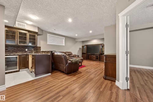 Spacious finished basement featuring wood-finish flooring, recessed lighting, and a built-in wet bar with glass-front cabinetry and an integrated beverage refrigerator - 1254 Adamson Drive, Edmonton, AB - Indoor