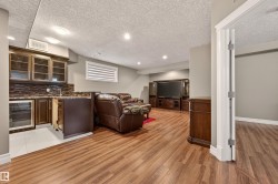 Spacious finished basement featuring wood-finish flooring, recessed lighting, and a built-in wet bar with glass-front cabinetry and an integrated beverage refrigerator - 