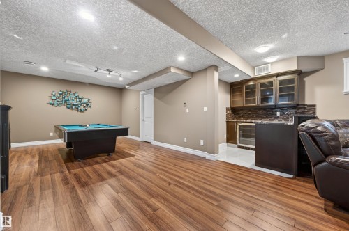 Spacious recreation room featuring wood-finish flooring, recessed lighting, and a built-in wet bar with a tile backsplash and under-counter refrigerator - 1254 Adamson Drive, Edmonton, AB - Indoor Photo Showing Other Room