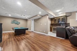 Spacious recreation room featuring wood-finish flooring, recessed lighting, and a built-in wet bar with a tile backsplash and under-counter refrigerator - 