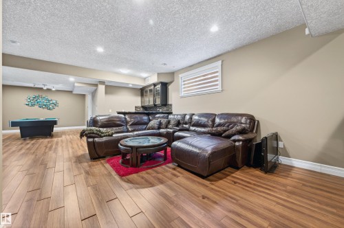 Spacious open-concept lower level with wood-finish flooring, recessed lighting, and a built-in wet bar featuring dark cabinetry and a stone-finish countertop - 1254 Adamson Drive, Edmonton, AB - Indoor