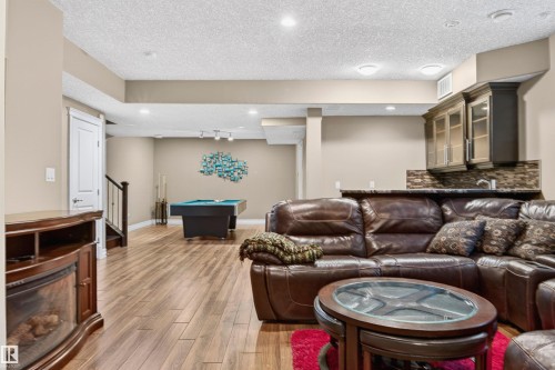 Spacious lower level featuring wood-finish flooring, recessed lighting, and a built-in wet bar with dark cabinetry and a tile backsplash - 1254 Adamson Drive, Edmonton, AB - Indoor Photo Showing Living Room With Fireplace