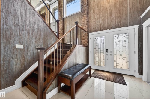 Grand foyer featuring a stained wood staircase with wrought iron balusters, stone accent wall, decorative double entry doors, and tile flooring - 1254 Adamson Drive, Edmonton, AB - Indoor Photo Showing Other Room