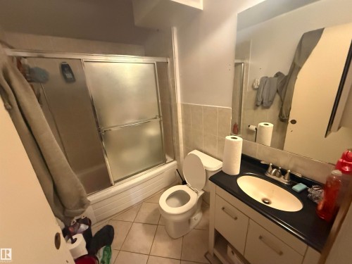 This bathroom features a shower and tub combination with sliding glass doors, a vanity with an integrated sink, and tiled flooring - 10545 67 Avenue, Edmonton, AB - Indoor Photo Showing Bathroom