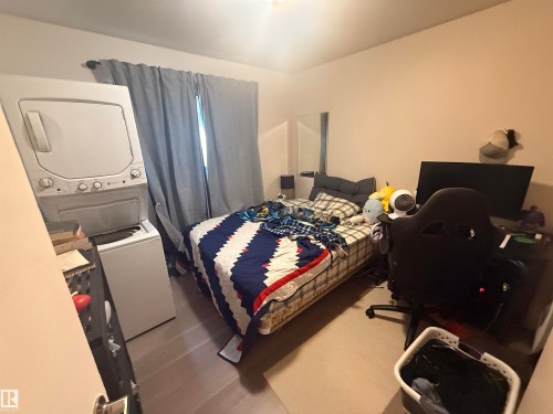 This room offers hard surface flooring, a window with curtains, and a stacked washer and dryer unit - 10545 67 Avenue, Edmonton, AB - Indoor Photo Showing Bedroom