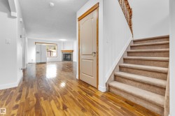 Hardwood-finish flooring extending from the entryway into the living area, featuring a carpeted staircase with a wood-finish banister, a white fireplace with a wood mantle, and white interior doors with wood trim - 