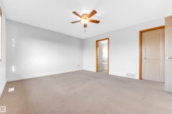 Spacious interior room featuring light neutral wall paint, light-colored carpeting, and a ceiling fan with light fixture - 