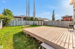 Expansive backyard featuring a large wood-finish deck, a detached storage shed, a fully fenced perimeter, and a generous grass area - 