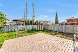 Expansive backyard featuring a spacious wooden deck, manicured lawn, full privacy fencing, and a functional storage shed - 