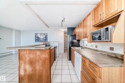 Kitchen featuring wood cabinetry, laminate countertops, stainless steel sink, built-in microwave, and tile flooring - 405 10135 Saskatchewan Drive Nw, Edmonton, AB - Indoor Photo Showing Kitchen With Double Sink