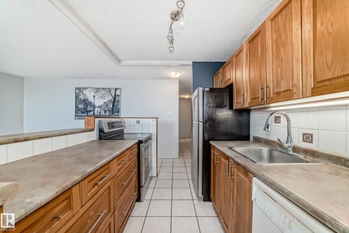 Kitchen featuring wood cabinetry, stainless steel sink with pull-down faucet, white tiled backsplash, and neutral countertops - 405 10135 Saskatchewan Drive Nw, Edmonton, AB - Indoor Photo Showing Kitchen
