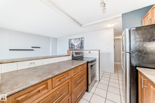 Kitchen featuring wood-finish cabinetry, solid surface countertops, a white tile backsplash, and tile flooring - 405 10135 Saskatchewan Drive Nw, Edmonton, AB - Indoor Photo Showing Kitchen