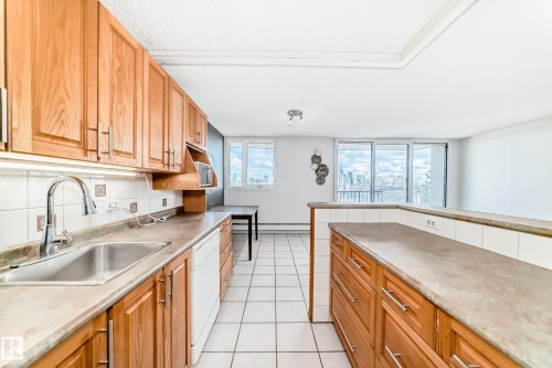 Kitchen featuring wood cabinetry, white tile backsplash, a stainless steel sink, and a white dishwasher - 405 10135 Saskatchewan Drive Nw, Edmonton, AB - Indoor Photo Showing Kitchen