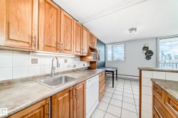 Kitchen featuring wood cabinetry, a stainless steel sink with a gooseneck faucet, a white tile backsplash with decorative accents, and tiled flooring - 