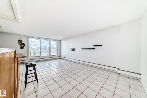 Spacious living area featuring large sliding glass doors, cityscape scenery, tile flooring, and a built-in wood-finish bar - 405 10135 Saskatchewan Drive Nw, Edmonton, AB - Indoor Photo Showing Other Room