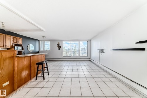 Spacious interior featuring a built-in wood-finish bar with upper cabinetry, large tile flooring, and expansive windows offering distant cityscape views - 405 10135 Saskatchewan Drive Nw, Edmonton, AB - Indoor