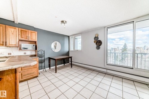 Kitchen and dining area featuring ceramic tile flooring, wood cabinetry, built-in microwave, and large sliding glass doors opening to a balcony - 405 10135 Saskatchewan Drive Nw, Edmonton, AB - Indoor Photo Showing Kitchen