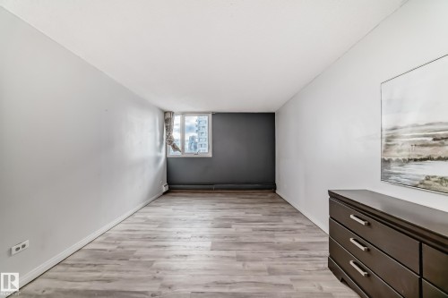 Spacious room featuring wood-finish flooring, a prominent window, a contrasting accent wall, light-toned walls, and white baseboards - 405 10135 Saskatchewan Drive Nw, Edmonton, AB - Indoor Photo Showing Other Room