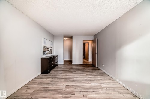 Spacious interior room featuring wood-finish flooring, light gray wall tones, white baseboards, and a textured ceiling - 405 10135 Saskatchewan Drive Nw, Edmonton, AB - Indoor Photo Showing Other Room