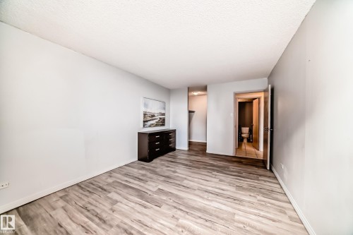 Expansive room featuring wood-finish flooring, light gray walls, white baseboards, and a textured white ceiling - 405 10135 Saskatchewan Drive Nw, Edmonton, AB - Indoor