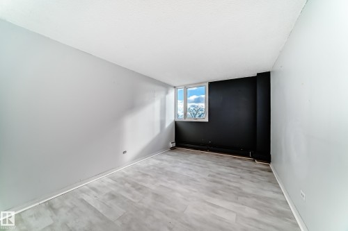 Spacious room featuring light wood-finish flooring, a contemporary black accent wall, and three large windows - 405 10135 Saskatchewan Drive Nw, Edmonton, AB - Indoor Photo Showing Other Room