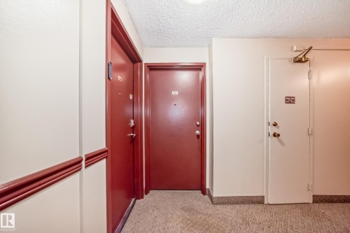 Common area hallway featuring two red-painted entry doors and one white utility door - 405 10135 Saskatchewan Drive Nw, Edmonton, AB - Indoor Photo Showing Other Room