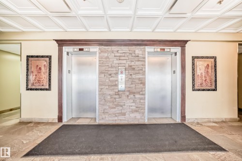 Dual elevators with brushed metal doors framed by substantial wood trim and stone veneer - 405 10135 Saskatchewan Drive Nw, Edmonton, AB - Indoor Photo Showing Other Room