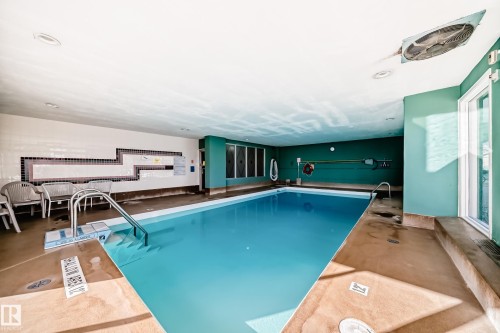Indoor swimming pool featuring a light blue tiled basin with metal grab rails - 405 10135 Saskatchewan Drive Nw, Edmonton, AB - Indoor Photo Showing Other Room With In Ground Pool