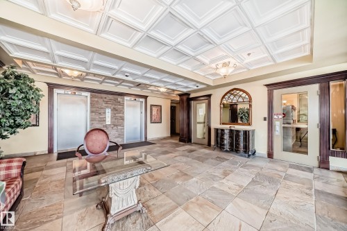 Spacious common area featuring textured tile flooring, two elevators with stone surround, a coffered ceiling, and dark wood trim accents - 405 10135 Saskatchewan Drive Nw, Edmonton, AB - Indoor Photo Showing Other Room