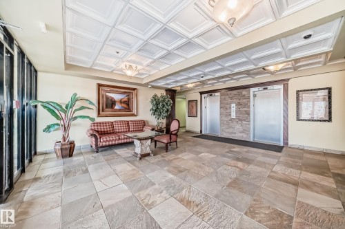 Spacious common area featuring natural stone flooring, a coffered ceiling with integrated lighting, and dual elevators with a stone accent wall - 405 10135 Saskatchewan Drive Nw, Edmonton, AB - Indoor Photo Showing Other Room