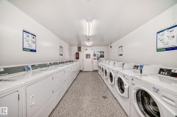 Dedicated laundry facility featuring multiple front-loading and top-loading machines, fluorescent overhead lighting, and durable speckled flooring - 