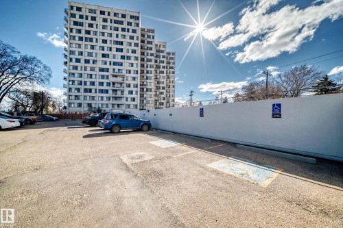 Asphalt parking lot featuring designated accessible parking spaces and a white privacy wall - 405 10135 Saskatchewan Drive Nw, Edmonton, AB - Outdoor