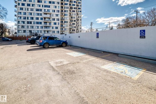 Paved parking area with marked spaces and concrete barriers, featuring a tall, multi-story building in the background - 405 10135 Saskatchewan Drive Nw, Edmonton, AB - Outdoor