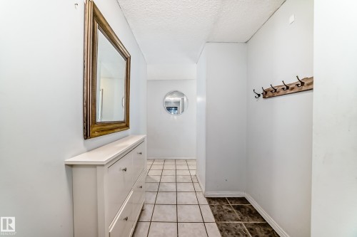 Hallway featuring square tile flooring, a wall-mounted coat rack, and a decorative round mirror - 405 10135 Saskatchewan Drive Nw, Edmonton, AB - Indoor Photo Showing Other Room