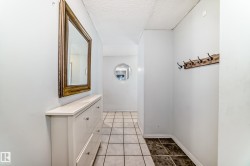Hallway featuring square tile flooring, a wall-mounted coat rack, and a decorative round mirror - 
