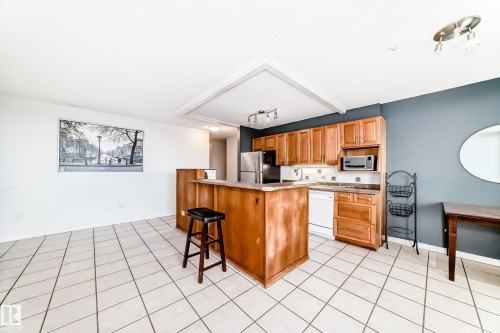 Open-concept kitchen featuring wood cabinetry, white tile flooring, stainless steel refrigerator, and integrated microwave - 405 10135 Saskatchewan Drive Nw, Edmonton, AB - Indoor Photo Showing Kitchen
