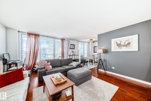 Spacious living area featuring polished wood-finish flooring, a full wall of windows with balcony access, and a distinct accent wall - 601 10135 Saskatchewan Drive Nw, Edmonton, AB - Indoor Photo Showing Living Room