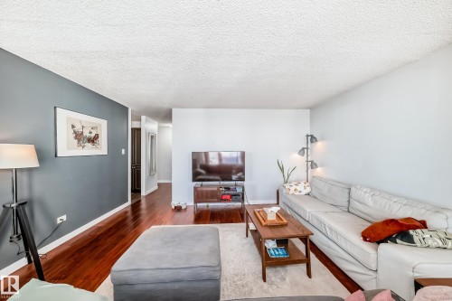Open-concept living space featuring wood-finish flooring, a wall with contrasting paint, and a textured white ceiling - 601 10135 Saskatchewan Drive Nw, Edmonton, AB - Indoor Photo Showing Living Room