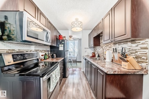 Galley kitchen featuring dark wood cabinetry, stainless steel appliances, wood-finish flooring, and a stone-finish countertop - 601 10135 Saskatchewan Drive Nw, Edmonton, AB - Indoor Photo Showing Kitchen With Double Sink With Upgraded Kitchen