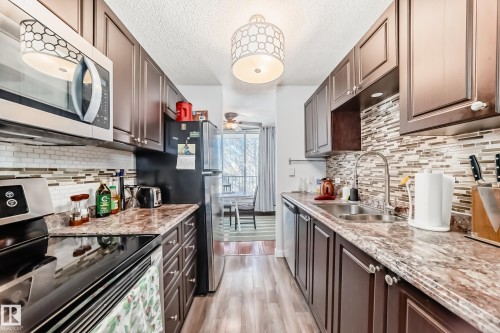 Galley kitchen featuring wood-finish cabinetry, granite-look countertops, and an integrated mosaic tile backsplash - 601 10135 Saskatchewan Drive Nw, Edmonton, AB - Indoor Photo Showing Kitchen With Double Sink With Upgraded Kitchen