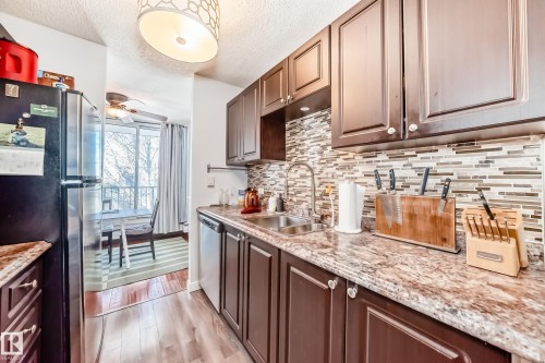 Kitchen featuring wood-finish flooring, dark wood cabinetry, a mosaic tile backsplash, and stone-look countertops - 601 10135 Saskatchewan Drive Nw, Edmonton, AB - Indoor Photo Showing Kitchen With Double Sink With Upgraded Kitchen