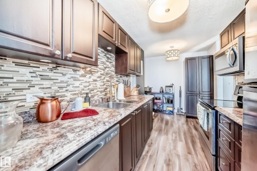 Kitchen featuring wood-finish flooring, dark wood cabinetry, a tiled backsplash, and stone-finish countertops - 601 10135 Saskatchewan Drive Nw, Edmonton, AB - Indoor Photo Showing Kitchen With Double Sink With Upgraded Kitchen