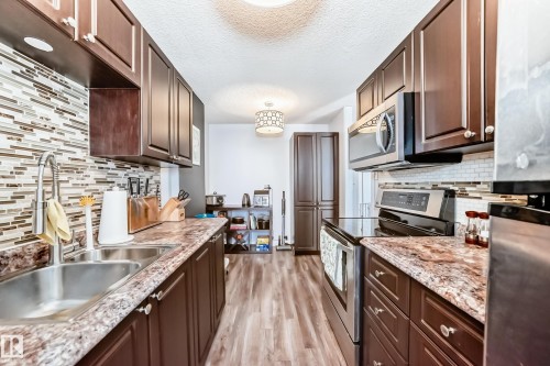 Galley kitchen featuring wood-finish flooring, dark wood cabinetry, and speckled countertops - 601 10135 Saskatchewan Drive Nw, Edmonton, AB - Indoor Photo Showing Kitchen With Double Sink