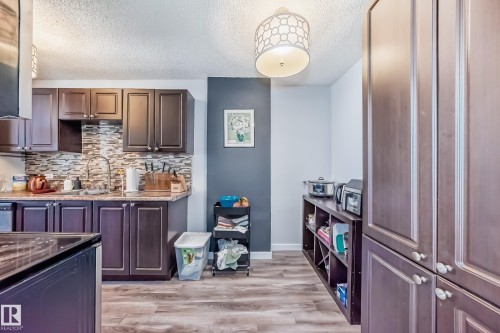 Kitchen featuring dark wood-finish cabinetry, a mosaic tile backsplash, a gooseneck faucet, and wood-finish flooring - 601 10135 Saskatchewan Drive Nw, Edmonton, AB - Indoor Photo Showing Kitchen