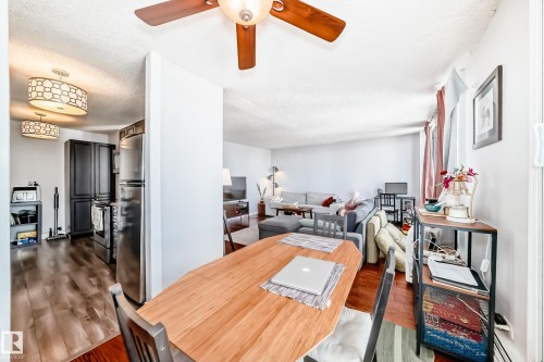 Open-concept living space featuring wood-finish flooring, a contemporary ceiling fan with integrated lighting, and a modern kitchen with dark cabinetry and stainless steel appliances - 601 10135 Saskatchewan Drive Nw, Edmonton, AB - Indoor