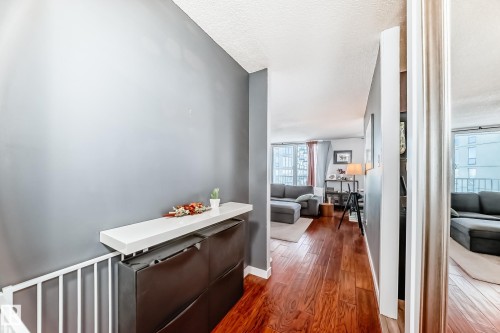 Hallway featuring wood-finish flooring, a white floating shelf, and a partial view into a living area with large windows - 601 10135 Saskatchewan Drive Nw, Edmonton, AB - Indoor Photo Showing Other Room