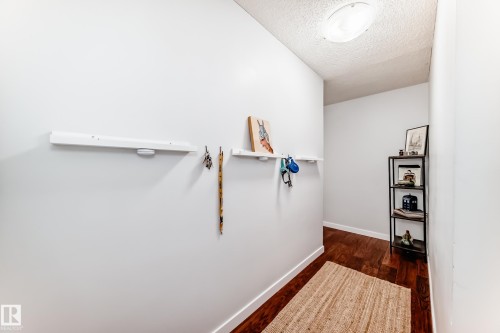 Hallway featuring wood-finish flooring, white baseboards, a built-in shelf with hooks, and a flush-mount ceiling light - 601 10135 Saskatchewan Drive Nw, Edmonton, AB - Indoor