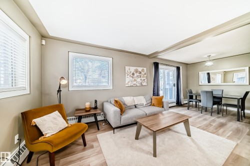 Open concept living and dining area featuring wood-finish flooring, multiple windows with blinds, a sliding glass door, and a dining space with an overhead light fixture - 101 10827 85 Avenue Nw, Edmonton, AB - Indoor Photo Showing Living Room