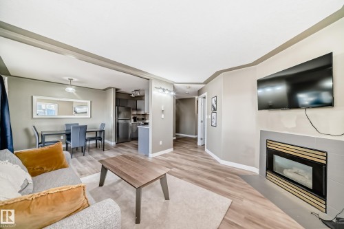 Open-concept living area featuring wood-finish flooring, a contemporary fireplace with a tiled surround, recessed lighting, and a dining space with an overhead fixture - 101 10827 85 Avenue Nw, Edmonton, AB - Indoor Photo Showing Living Room With Fireplace