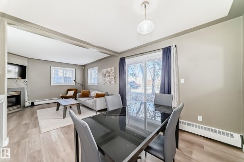 Open-concept living and dining areas featuring wood-finish flooring, a contemporary fireplace, and sliding glass doors leading to the exterior - 101 10827 85 Avenue Nw, Edmonton, AB - Indoor Photo Showing Dining Room With Fireplace